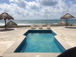 a swimming pool next to the ocean with chairs and umbrellas at Casa Amor Pto Morelos in Puerto Morelos