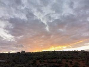 a cloudy sky with the sun setting on a hill at 1Happy farm in Al Salt
