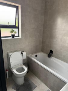 een badkamer met een toilet, een bad en een raam bij The Grey Luxe Suite in Sandton