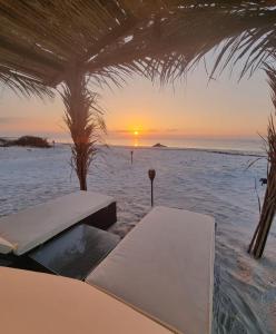 Een zonsondergang op het strand met twee tafels en een parasol van stro. bij Beach Moments Camp in Aḑyūḩ