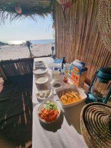 een tafel met schalen vol fruit en groenten op het strand bij Beach Moments Camp in Aḑyūḩ