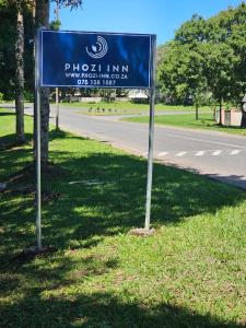een blauw bord in het gras naast een weg bij Phozi Inn in Eshowe