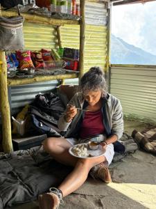 a woman sitting on the ground with a bowl of food at Thatharana Trek by Mountain Hikers - Mudhouse & Cafe in Dharmsāla