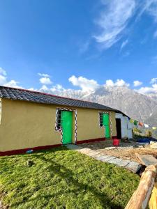 a house with green doors and mountains in the background at Thatharana Trek by Mountain Hikers - Mudhouse & Cafe in Dharmsāla