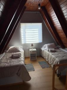ein Schlafzimmer im Dachgeschoss mit zwei Betten und einem Fenster in der Unterkunft Cabañas Alpinas M&M in Perito Moreno