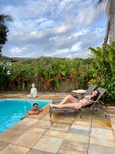 Twee mensen liggen op stoelen bij een zwembad. bij Casa da Tartaruga Búzios in Búzios