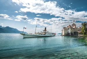 a boat in the water next to a castle at La Suite du Bourg in La Tour-de-Peilz