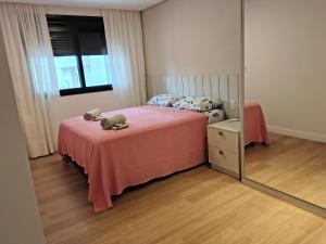 een slaapkamer met een roze bed en een spiegel bij Sinta se em casa, mas, com sol e mar in Torres