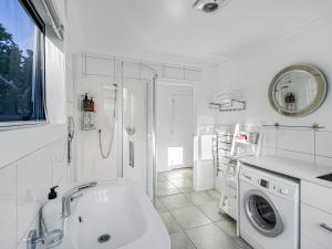 een witte badkamer met een wastafel en een wasmachine bij Cosy Guesthouse in Tranquil Puriri, Thames in Thames