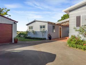 een wit huis met een garage en een oprit bij Cosy Guesthouse in Tranquil Puriri, Thames in Thames