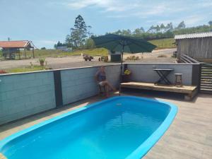 a man sitting under an umbrella next to a swimming pool at Bella montanha pousada e camping in Lauro Müller