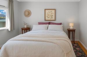 een slaapkamer met een groot wit bed en 2 tafels bij Plum Coastal Cottage in Raumati Beach