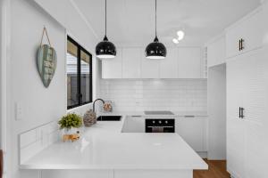 een witte keuken met een wit aanrechtblad en zwarte hanglampen bij Henderson Oasis in Auckland