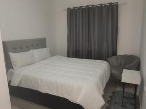 een slaapkamer met een wit bed en een stoel bij The Nexus Suites in Gaborone
