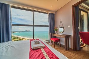 a bedroom with a bed and a desk and a large window at APEC Mandala Mũi Né VIP in Mui Ne