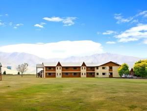 a large building in a field with mountains in the background at Discovery Countrytime Hotel Omarama in Omarama