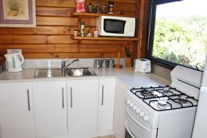 Il comprend une cuisine blanche équipée d'une cuisinière et d'un four micro-ondes. dans l'établissement Lavendula Garden Cottage, à Burnt Pine