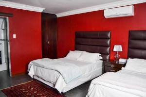 twee bedden in een kamer met een rode muur bij Casadeross Guest House in Pretoria