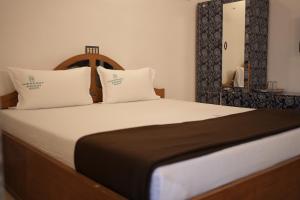 una camera da letto con un letto con lenzuola bianche e uno specchio di Thekkady Arasi Hotel a Thekkady Altre 31 foto