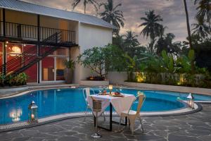 een tafel en stoelen naast een zwembad bij LaRiSa Resort, Morjim in Morjim