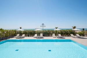 ein Swimmingpool mit Liegen und Sonnenschirmen und das Meer in der Unterkunft Vibra Tahiti Comfort in Lido di Jesolo + 4 Fotos