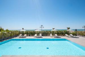 ein Swimmingpool mit Stühlen und das Meer im Hintergrund in der Unterkunft Vibra Tahiti Comfort in Lido di Jesolo