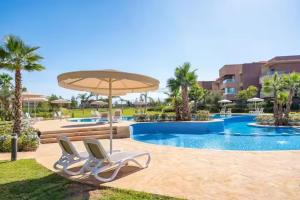 two chairs and an umbrella next to a swimming pool at appartement prestige golf city in Marrakech
