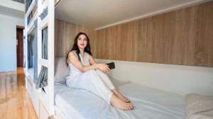 a woman sitting on a bed holding a remote control at Prestige holiday home Bed space in Dubai