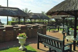 un groupe de bancs et de tables avec des parasols et l'océan dans l'établissement Inyoni Rocks Cabanas 15, à Amanzimtoti