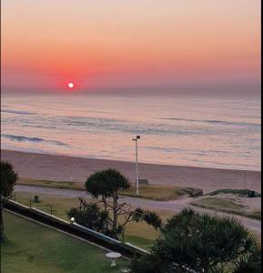 Een zonsondergang boven een strand met de oceaan en een straatlantaarn. bij Inyoni Rocks Cabanas 15 in Amanzimtoti