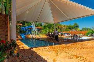 a man standing under an umbrella next to a swimming pool at Hotel Colonial Iguaçu in Foz do Iguaçu