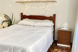 ein Schlafzimmer mit einem weißen Bett und einem Nachttisch in der Unterkunft Kitnet na rua da UFV com Smart TV e Garagem in Viçosa