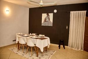 ParakouRésidences Fifamè的用餐室配有带白色椅子的桌子和绘画作品