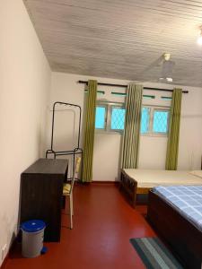 a room with a bed and a desk and two windows at Schanigarten in Deniyaya