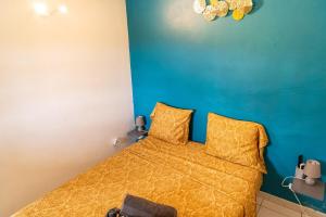a bedroom with a bed with yellow sheets and a blue wall at Bel La Vi Apartment in Le Lamentin