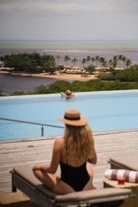 een vrouw met een hoed op een stoel naast een zwembad bij Bela Vista Hotel Boutique in Caraíva