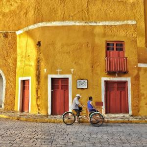Twee mensen fietsen voor een geel gebouw. bij Casa Guacamaya in Izamal