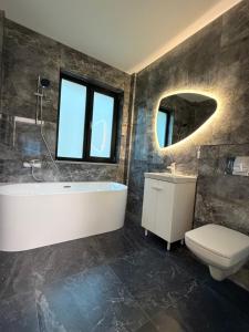 een badkamer met een bad, een toilet en een spiegel bij Altheda Living Stejari 4B in Suceava