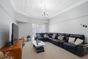 a living room with a black leather couch and a tv at Edwin Cottage Dubbo - close to the hospital in Dubbo