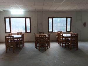 an empty room with tables and chairs and windows at Hotel Dharam Ganga in Uttarkāshi