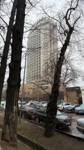 a tall building with cars parked in a parking lot at Kurmangazy in Zhezdi