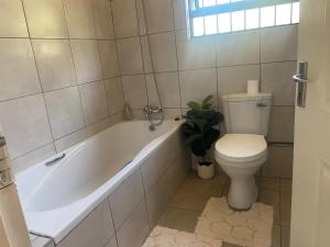 La salle de bains est pourvue d'une baignoire blanche, de toilettes et d'une plante. dans l'établissement Cozy Haven in Manzini, à Manzini