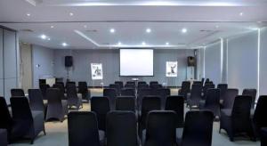 een vergaderzaal met zwarte stoelen en een scherm bij Hotel Dafam Pacific Caesar in Surabaya