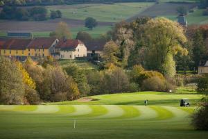 einen Golfer auf einem Grün mit einem Haus im Hintergrund in der Unterkunft Apartments Golfpark Schlossgut Sickendorf in Lauterbach