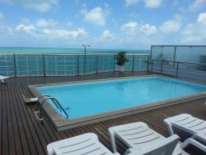 a swimming pool on a deck with chairs and the ocean at Manaíra Palace Residence in João Pessoa