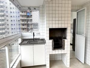 une cuisine carrelée de blanc avec un évier et un four dans l'établissement Apartmento com 3 dorm no Canto do Forte, à Praia Grande