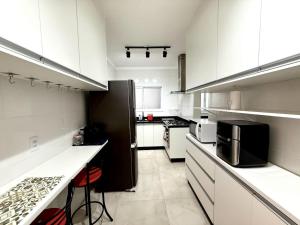 une cuisine avec des armoires blanches et un réfrigérateur noir dans l'établissement Apartmento com 3 dorm no Canto do Forte, à Praia Grande