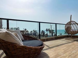 a basket chair on a balcony with a view of the ocean at מלון ארנה בת ים - קומת סוויטות הגן עם סאונה פרטית in Bat Yam