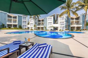 een zwembad met twee blauw-witte ligstoelen en een parasol bij Sterling Arka Suites, Puri in Puri