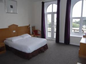 a bedroom with a bed and two large windows at Esplanade Hotel - Clacton On Sea, Beachfront Hotel by OYO in Clacton-on-Sea